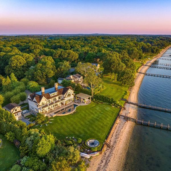 A large waterfront house with a green lawn and docks along the shoreline.