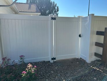 White vinyl fence with a gate and pink flowers in a rocky garden.