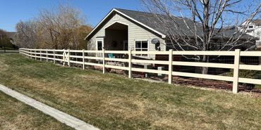A beige house with a white fence and leafless trees on a sunny day.