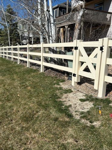 New white wooden fence with a gate in a suburban backyard on a sunny day.