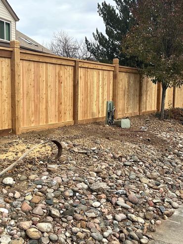 New wooden fence along a rocky landscaped sidewalk with trees.