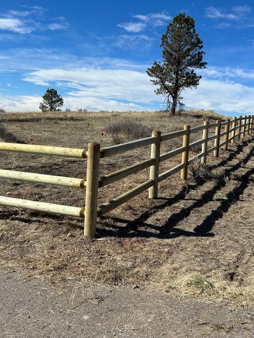 A long wooden fence casting shadows on dry grass under a blue sky.