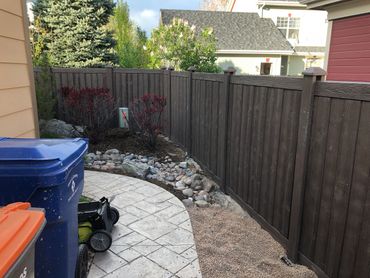 Backyard with trash bins, lawn mower, and wooden fence under a partly cloudy sky.