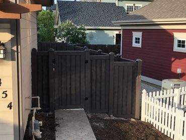 A black wooden fence gate with a tiled path leading to it.