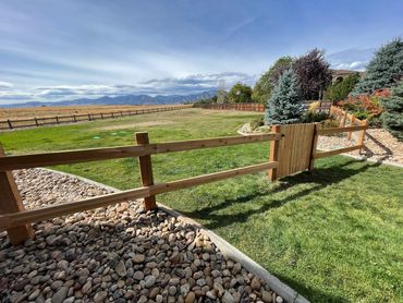 A wooden fence and gate enclosing a green lawn with mountains in the background.