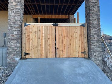 Wooden double gates with metal hinges under a covered structure.
