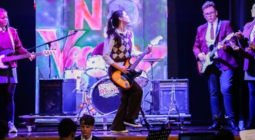 Students playing electric guitars and bass in front of drums