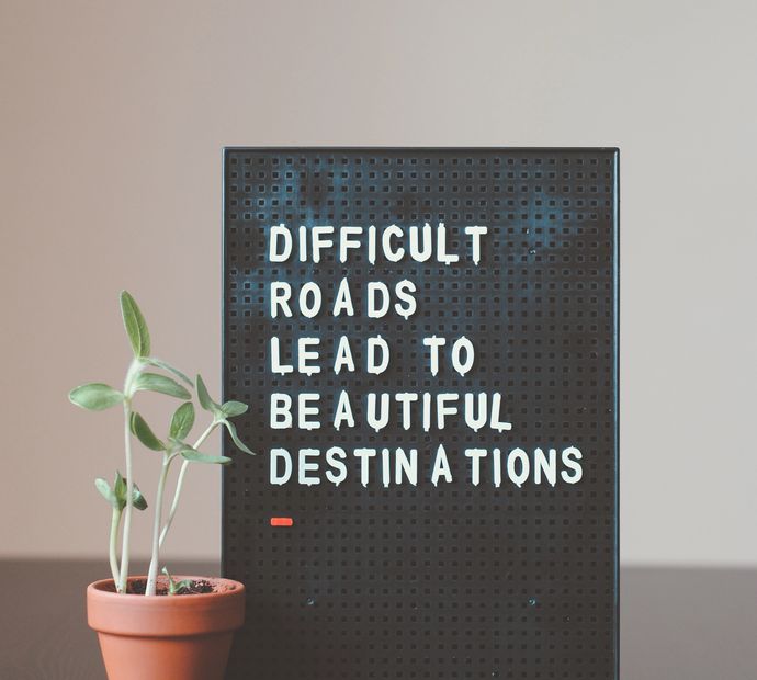 black pin board with text 'difficult roads lead to beautiful destinations' next to plant in pot