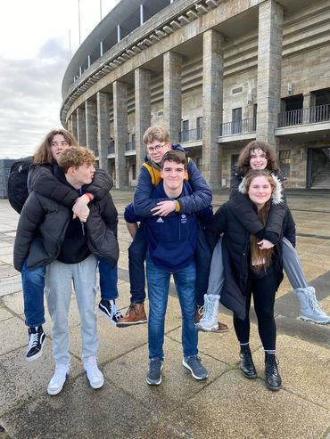 Three students giving piggyback rides to classmates outside the Berlin Olympic Stadium