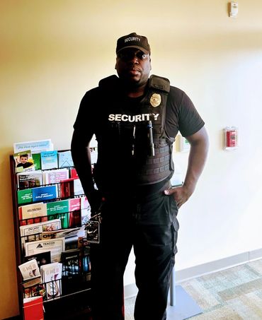 Security guard stands confidently in uniform near a rack of informational pamphlets indoors.