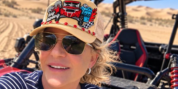 Woman wearing a hat and sunglasses in a desert area.