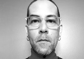 Black and white close-up portrait of a man wearing glasses.
