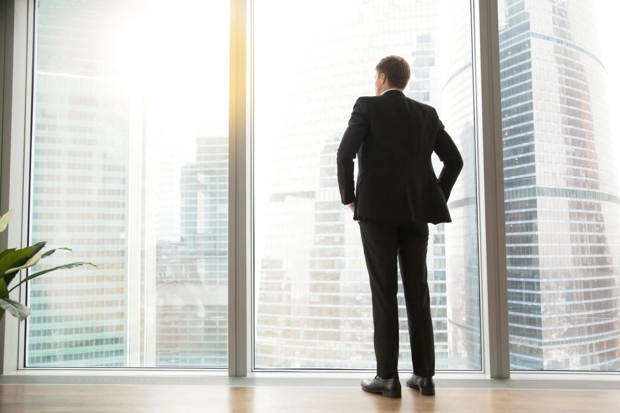 Businessman in suit looking out a large window at city buildings.