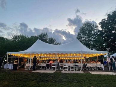 Outdoor evening event under a white tent with string lights.