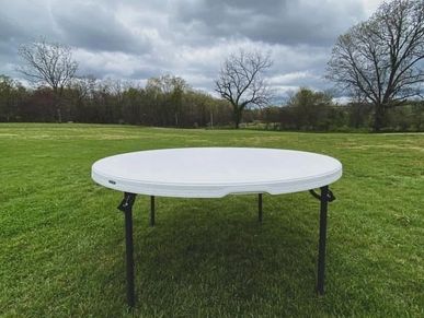 Round white folding table outdoors on grass.