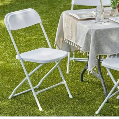White folding chair next to table on grass.