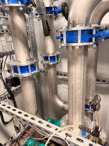 Industrial stainless steel pipes with blue flange connectors and valves inside a mechanical room.