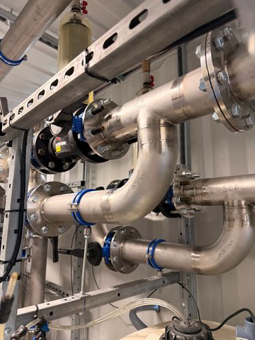 Industrial stainless steel pipes with flanges and blue clamps in a mechanical setup.