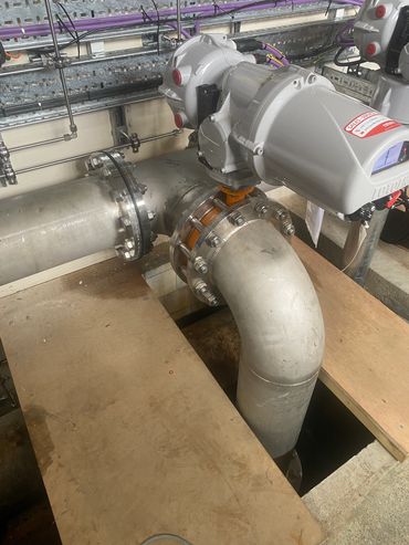 Industrial pipe system with large metal pipes and valve actuators in a mechanical room.