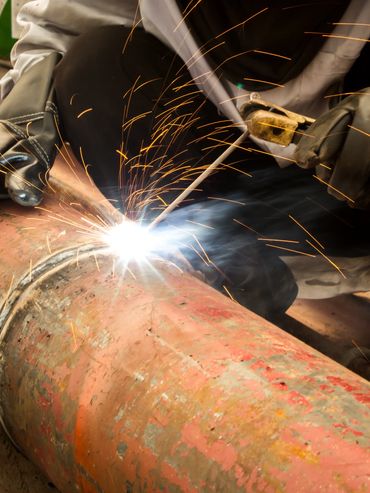A worker welding a rusty pipe with sparks flying.