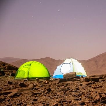 Two illuminated tents set up on rocky terrain under a starry night sky.