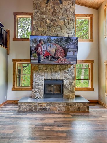 Stone fireplace with TV mounted above it in a spacious room with wooden floors.