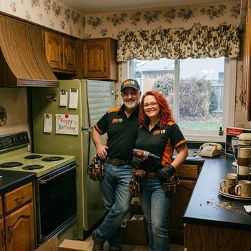 A couple in matching black and orange shirts with tools, standing in a vintage kitchen.