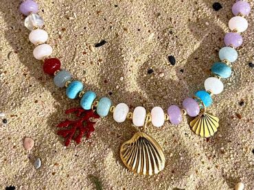Custom colorful beaded necklace with gold seashell and coral charms on sand.