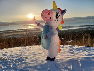 White unicorn with rainbow hair stands on snow overlooking Homer Spit