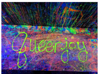 The words "queer joy" are written on a flat surface in neon green with neon paint splatters around