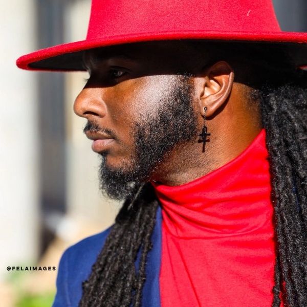 Man with long dreadlocks in a red hat and blue jacket.