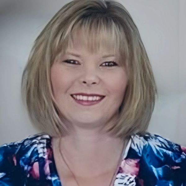 Smiling woman with blonde hair wearing a colorful blouse.