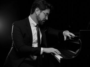 A man with a beard playing a baby grand piano