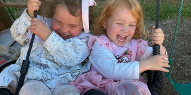 Two young girls laughing and swinging together on a swing.