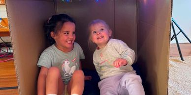 Two young children smiling inside a cardboard box.
