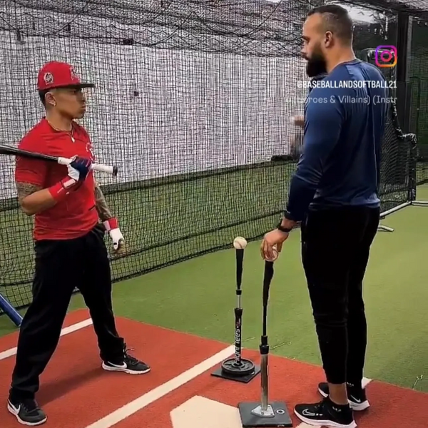 Two men in a batting cage practicing with baseball tees.