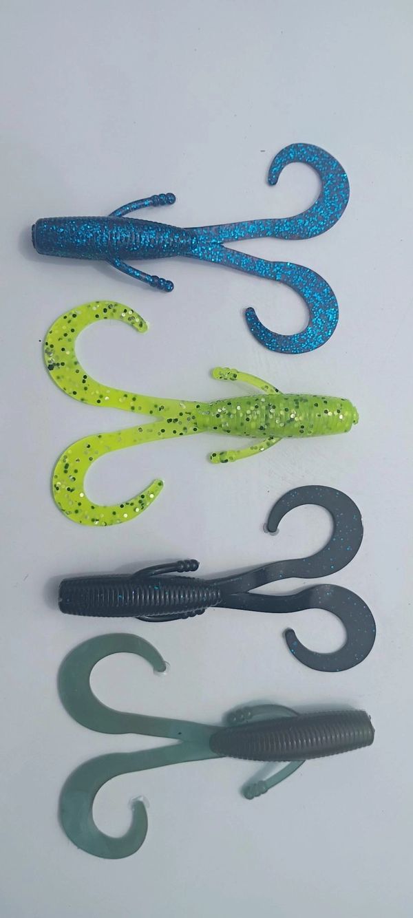 Four colorful soft plastic fishing lures with curly tails on a white background.