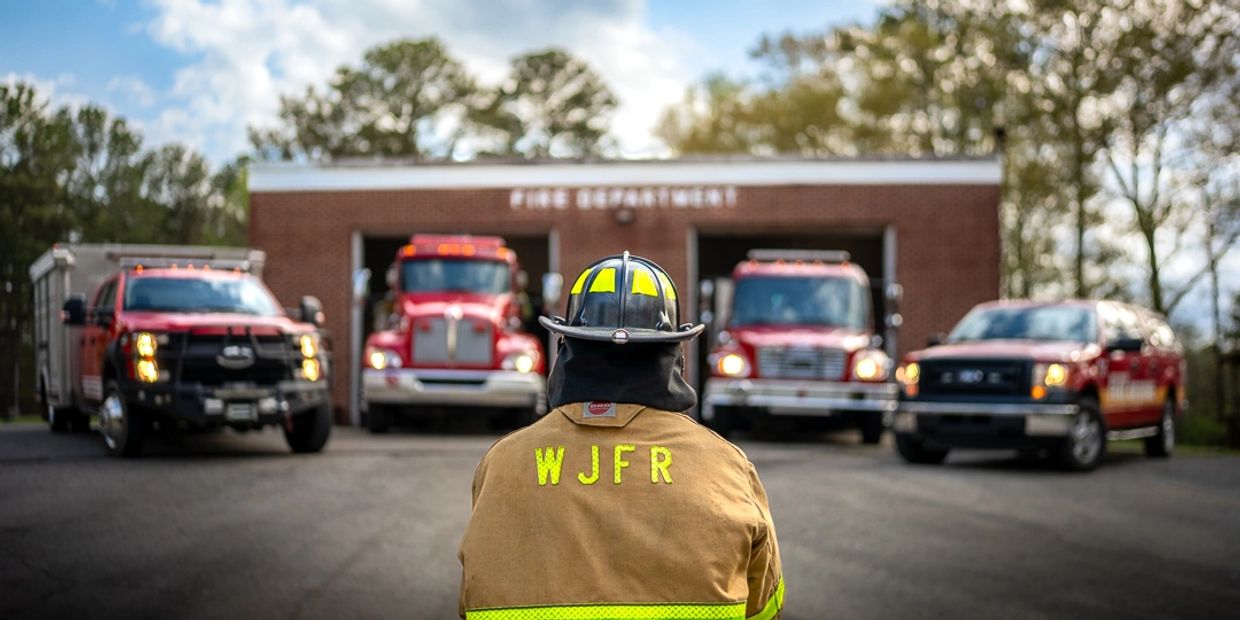Firefighter facing fire trucks outside fire station.