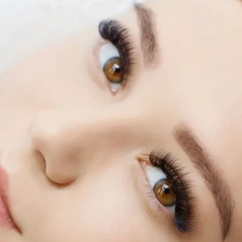 Close-up of a face highlighting brown eyes with long eyelashes and well-groomed eyebrows.
