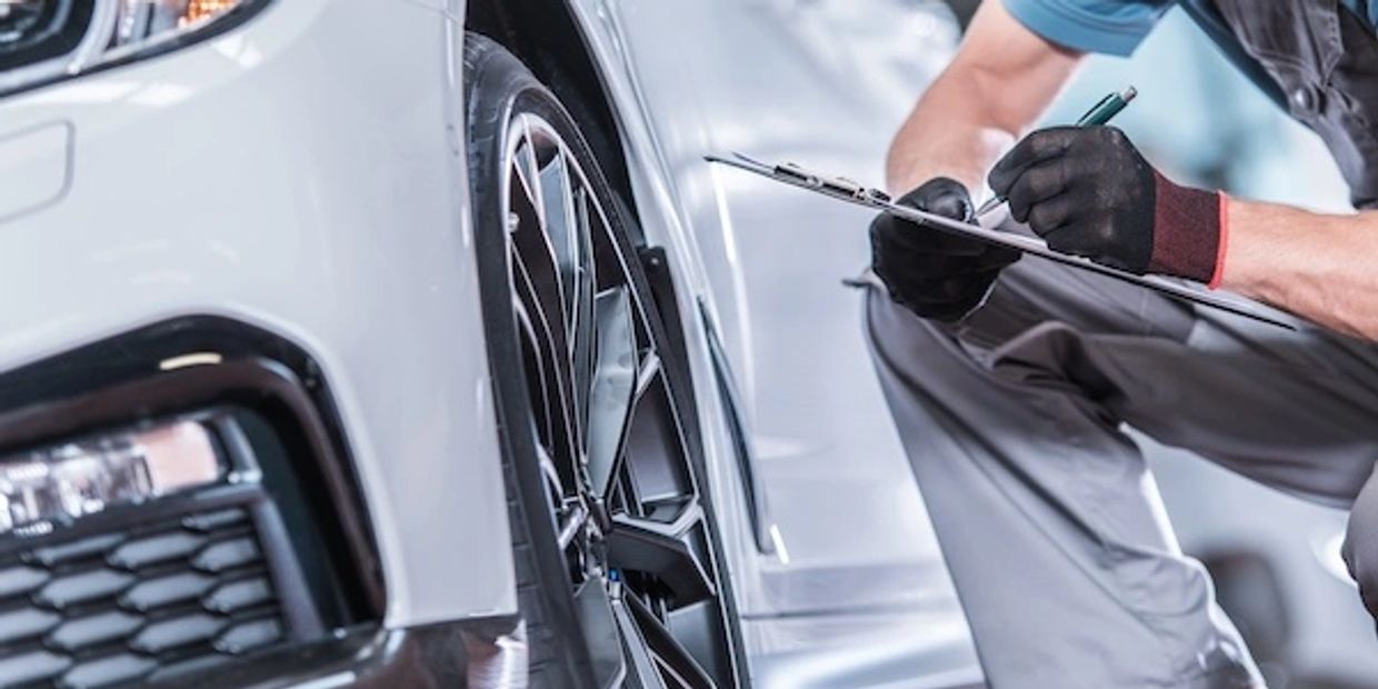 Mechanic inspecting a car wheel and taking notes.