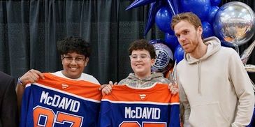 Two fans hold McDavid jerseys next to a man in a white hoodie.