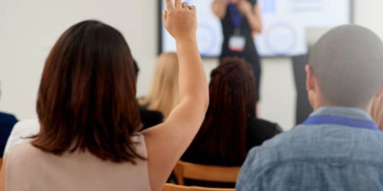 Person raising hand during a presentation in a seminar or classroom.