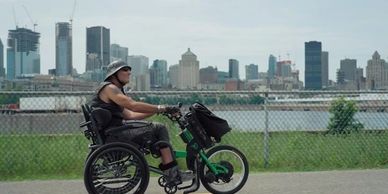 François sur son fauteuil motorisé sur le bord du fleuve avec la ville en arrière-plan