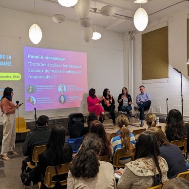 Image de la salle de l'événement avec le panel de spéclialistes en avant, les gens assis dans la sal