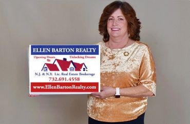 Woman holding a realty sign for Ellen Barton Realty with contact details.