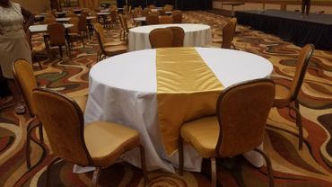 Round table with white and gold tablecloth in an empty event hall.