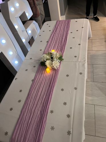 Table decorated with a purple runner, flowers, and candles.