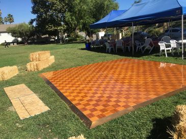 Outdoor event setup with tents, chairs, hay bales, and a wooden dance floor.