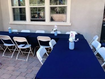 Outdoor tables with navy blue covers and white chairs set up for an event.