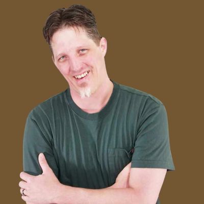 Occam smiling hugging himself in dark green shirt with brown background